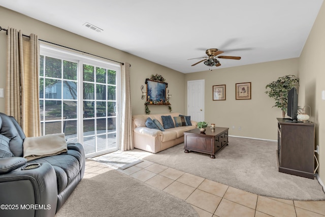 living area featuring light carpet, ceiling fan, light tile patterned flooring, and baseboards