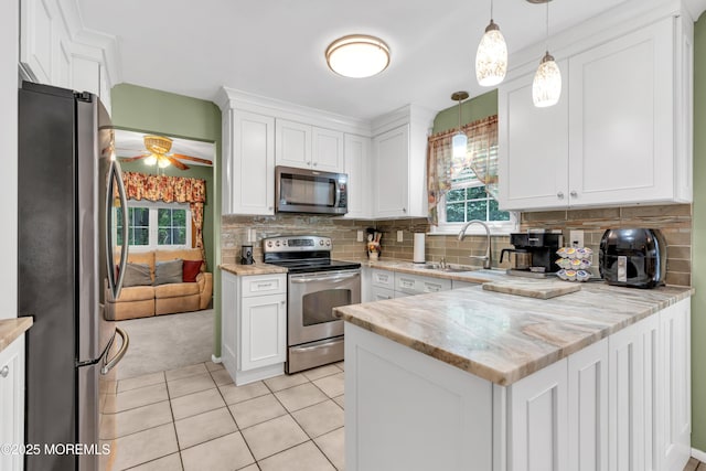 kitchen with appliances with stainless steel finishes, a sink, white cabinetry, a peninsula, and light tile patterned flooring
