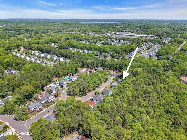 aerial view of property and surrounding area featuring a forest and nearby suburban area
