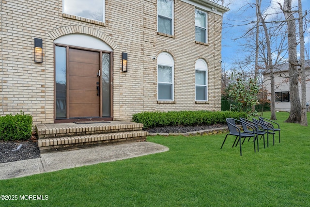 entrance to property featuring brick siding and a lawn