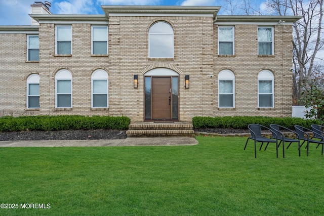 view of front of property featuring brick siding, a front yard, and a chimney