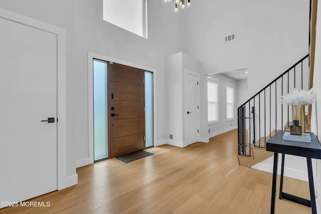 entrance foyer with light wood finished floors, baseboards, stairway, a chandelier, and a high ceiling