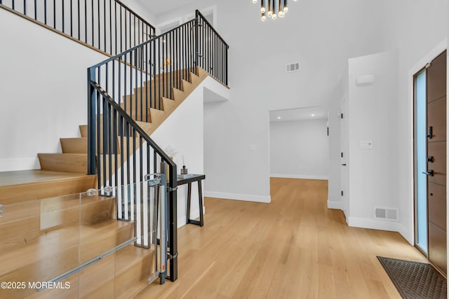 entrance foyer with baseboards, a towering ceiling, wood finished floors, stairs, and a chandelier