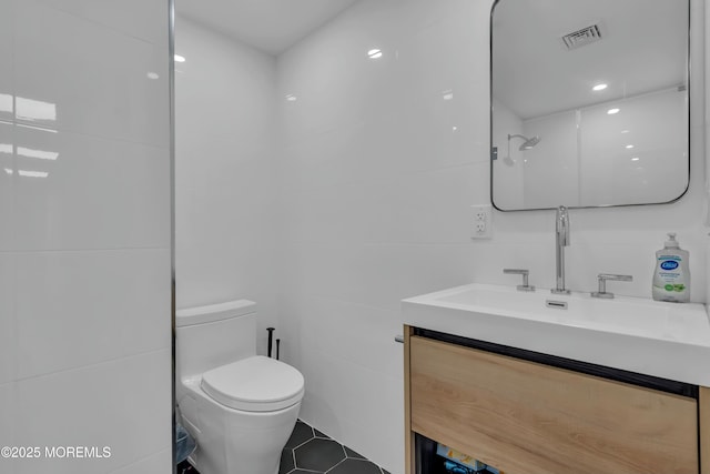 bathroom with toilet, tile walls, vanity, and tile patterned floors