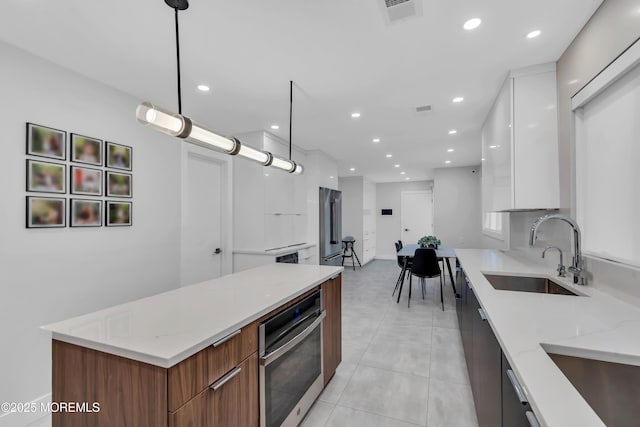 kitchen featuring modern cabinets, stainless steel oven, a sink, white cabinets, and recessed lighting
