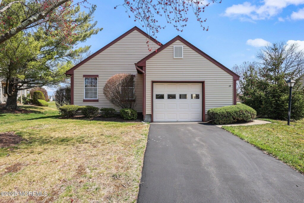 ranch-style home featuring an attached garage, a front lawn, and aphalt driveway