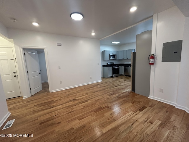 unfurnished living room with electric panel, light wood-style floors, visible vents, and baseboards