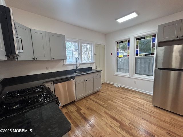 kitchen with stainless steel appliances, light wood-style floors, a sink, and dark countertops