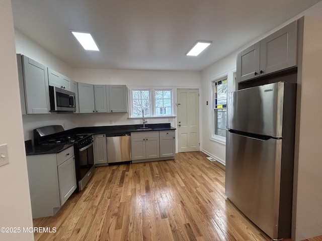 kitchen with a sink, dark countertops, light wood-style floors, stainless steel appliances, and gray cabinets