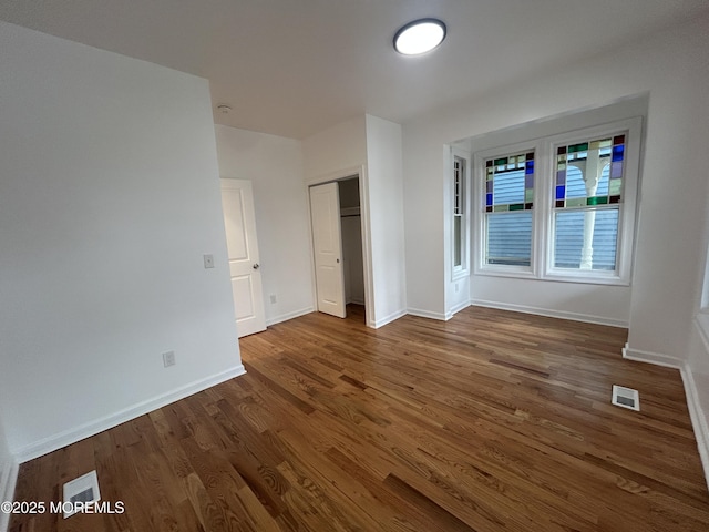 unfurnished bedroom with a closet, dark wood-style flooring, baseboards, and visible vents