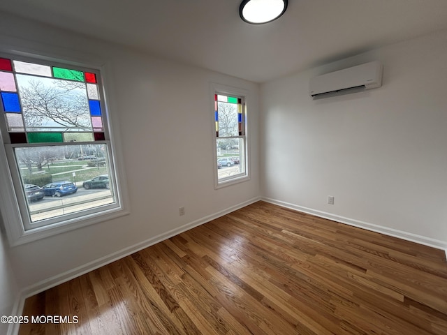spare room featuring an AC wall unit, baseboards, and wood finished floors