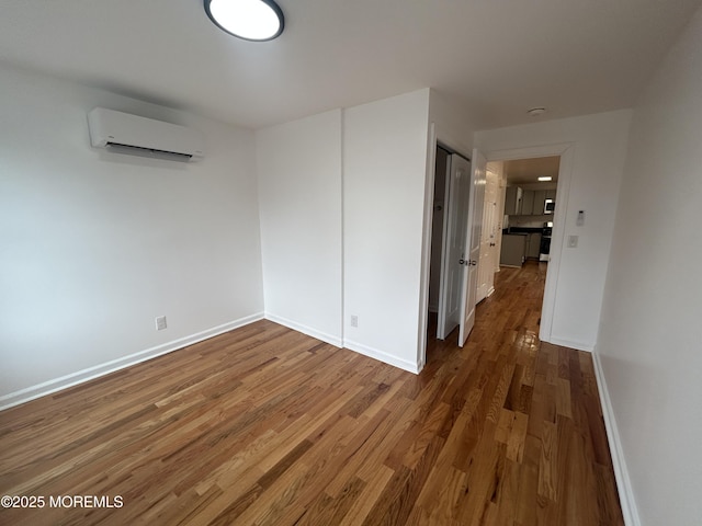 empty room featuring wood finished floors, baseboards, and an AC wall unit