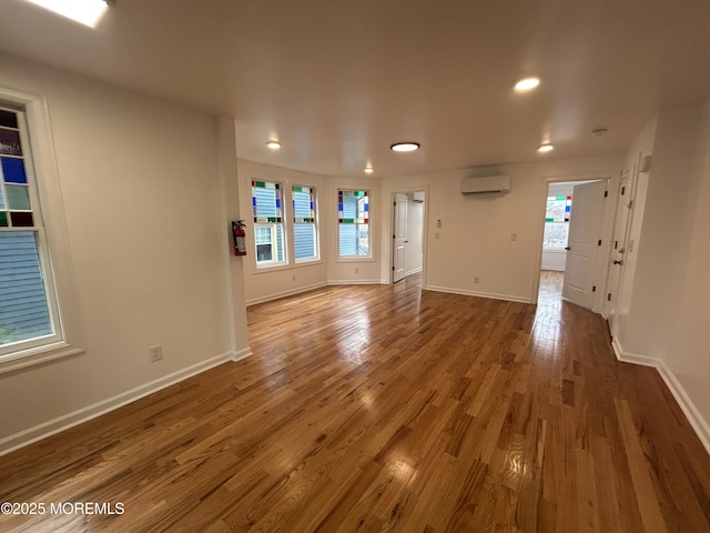 empty room featuring recessed lighting, an AC wall unit, baseboards, and wood finished floors