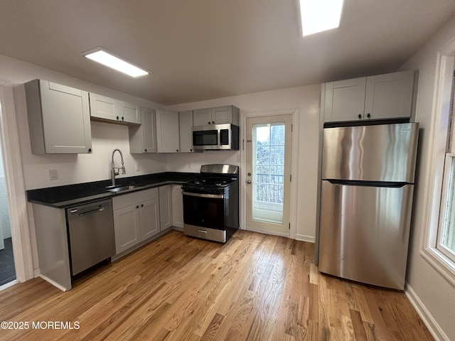 kitchen with baseboards, a sink, dark countertops, stainless steel appliances, and light wood-style flooring