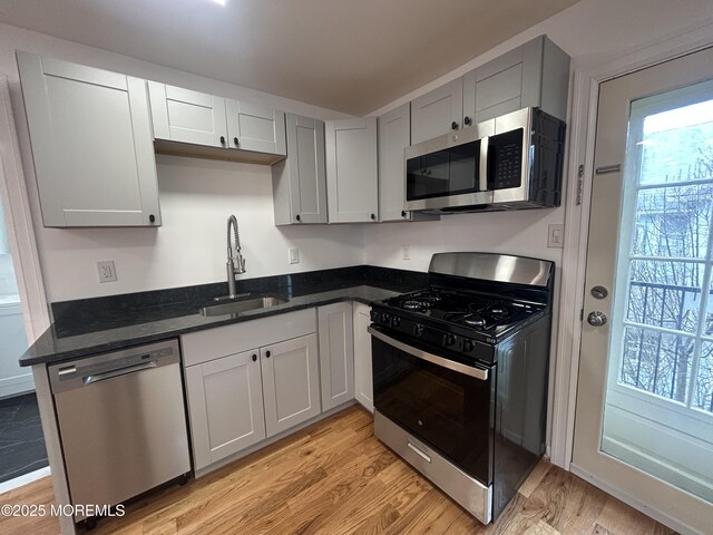 kitchen featuring light wood-style floors, dark stone counters, gray cabinets, appliances with stainless steel finishes, and a sink