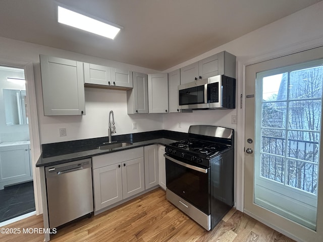 kitchen with a sink, gray cabinets, light wood-style flooring, and stainless steel appliances