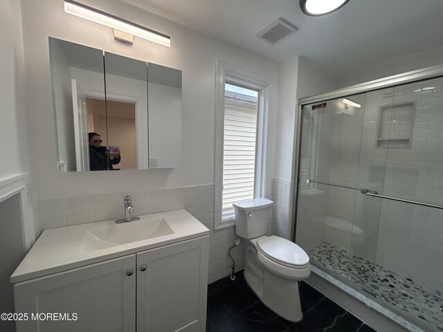 bathroom with vanity, a stall shower, toilet, visible vents, and tile walls