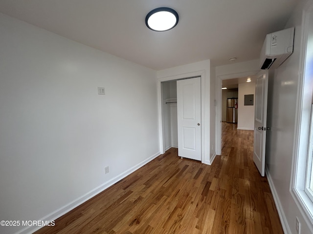 unfurnished bedroom with a closet, an AC wall unit, baseboards, freestanding refrigerator, and wood finished floors