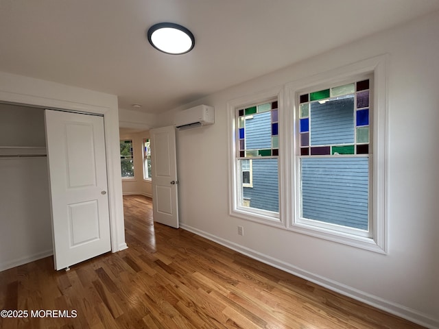 unfurnished bedroom with a closet, baseboards, wood finished floors, and a wall unit AC