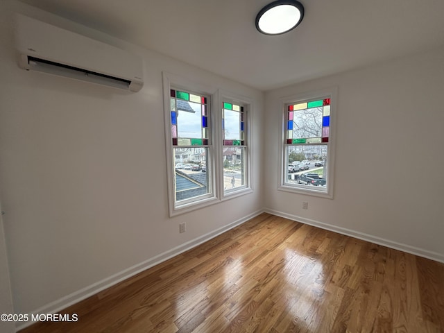 spare room featuring light wood-style flooring, a wall unit AC, and baseboards
