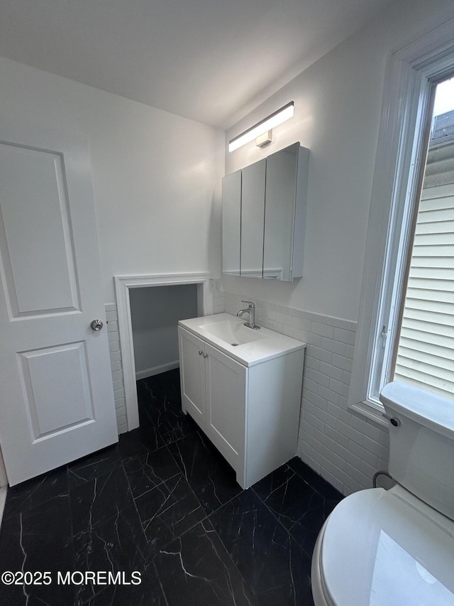bathroom featuring vanity, tile walls, toilet, wainscoting, and marble finish floor