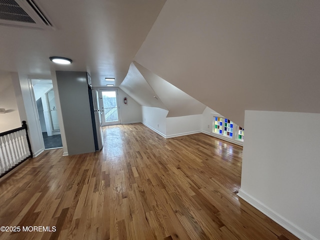 additional living space with wood finished floors, baseboards, vaulted ceiling, and visible vents