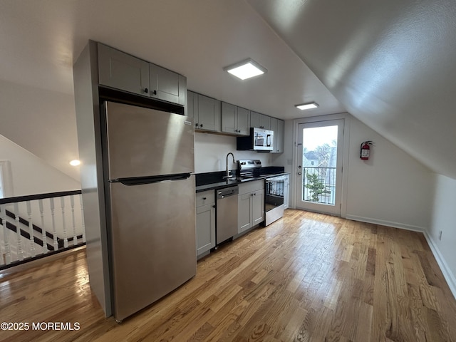 kitchen with stainless steel appliances, light wood-style flooring, a sink, and lofted ceiling