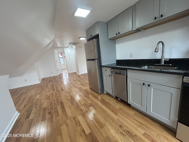 kitchen with a sink, appliances with stainless steel finishes, dark countertops, gray cabinetry, and light wood-style flooring