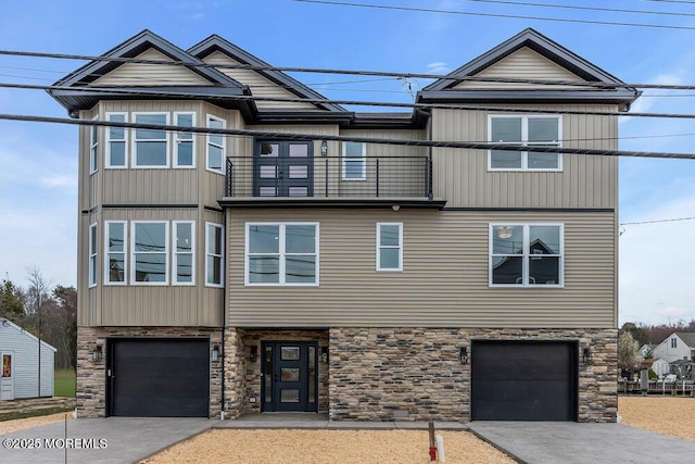 view of front of home featuring concrete driveway, a garage, stone siding, and a balcony