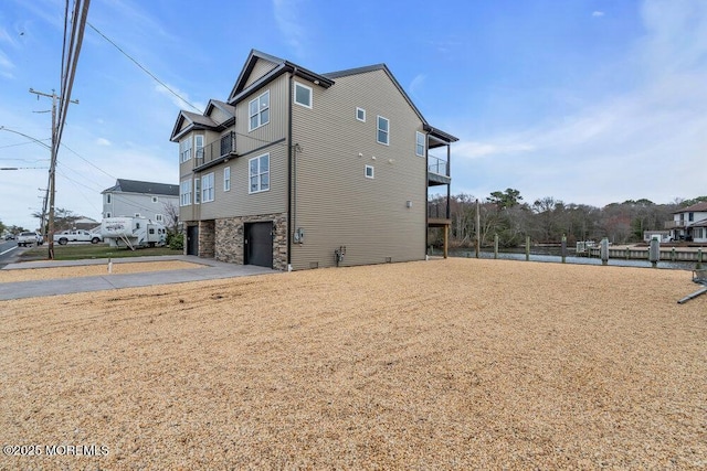 view of side of home featuring an attached garage, concrete driveway, and stone siding
