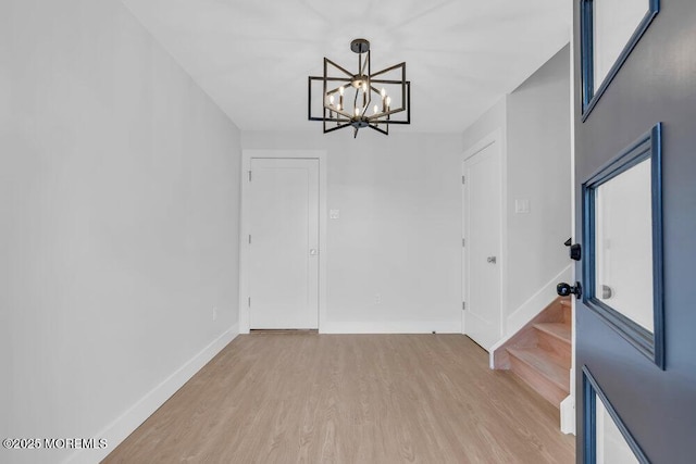 interior space featuring light wood-type flooring, an inviting chandelier, and baseboards