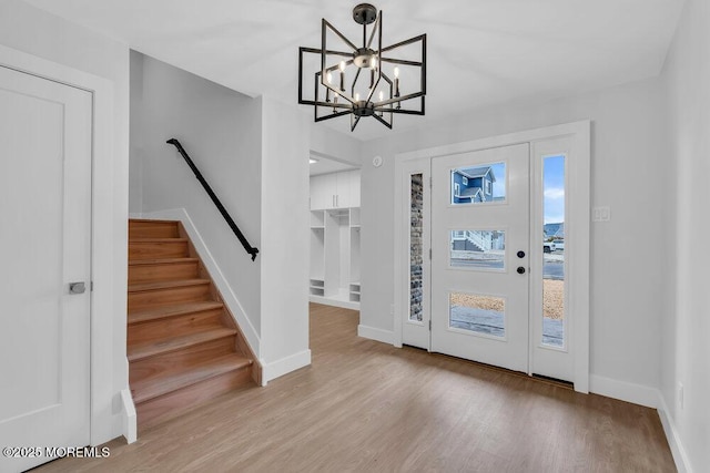 foyer entrance featuring baseboards, a notable chandelier, wood finished floors, and stairs