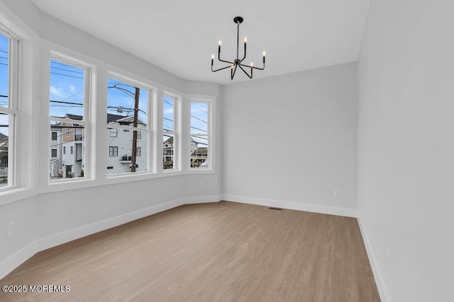 unfurnished dining area featuring a chandelier, baseboards, and wood finished floors