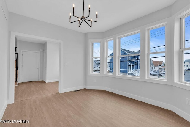 unfurnished dining area with plenty of natural light, light wood-style flooring, baseboards, and an inviting chandelier