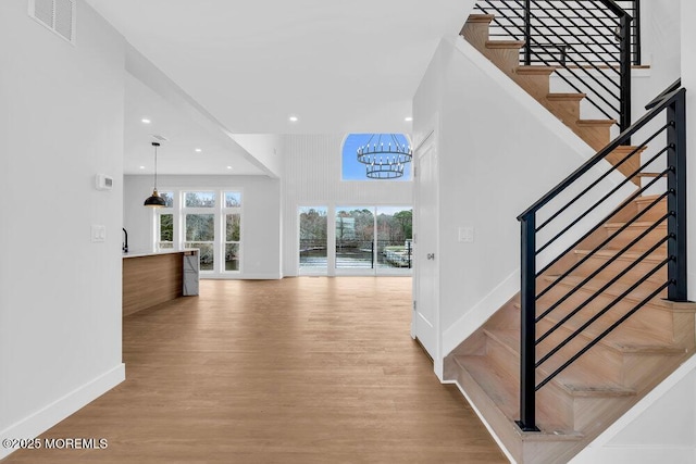 stairs featuring visible vents, baseboards, a chandelier, a towering ceiling, and wood finished floors