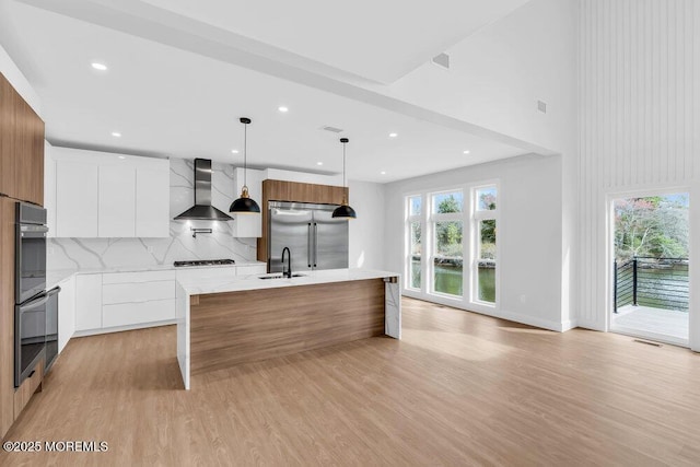 kitchen featuring modern cabinets, a sink, wall chimney range hood, stainless steel appliances, and backsplash