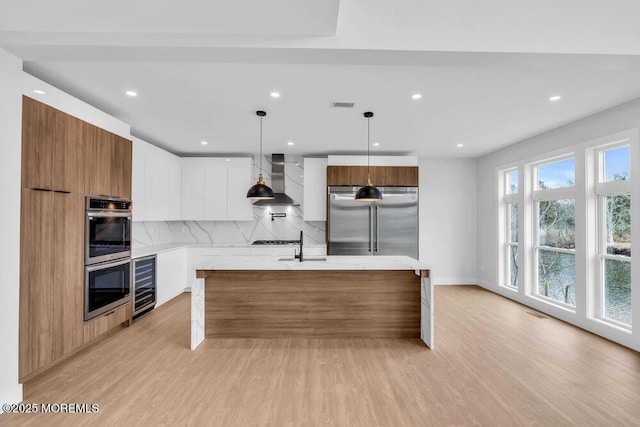 kitchen featuring visible vents, modern cabinets, wall chimney range hood, appliances with stainless steel finishes, and light wood finished floors