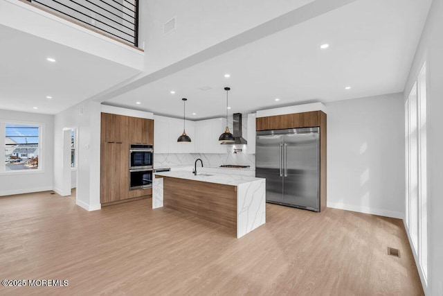 kitchen with modern cabinets, a sink, wall chimney range hood, appliances with stainless steel finishes, and brown cabinetry
