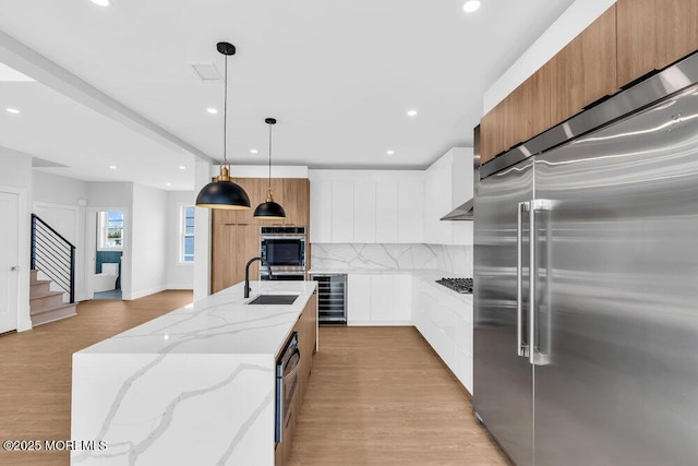 kitchen with modern cabinets, a sink, light wood-style floors, stainless steel appliances, and backsplash