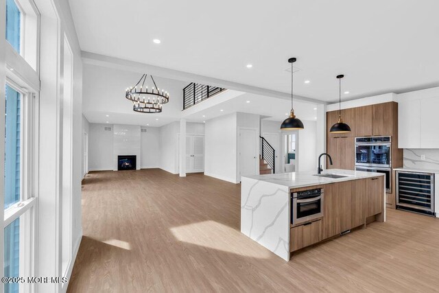 kitchen featuring modern cabinets, a sink, wine cooler, double oven, and light wood-style flooring