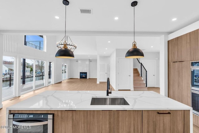kitchen with visible vents, modern cabinets, a sink, brown cabinetry, and stainless steel oven