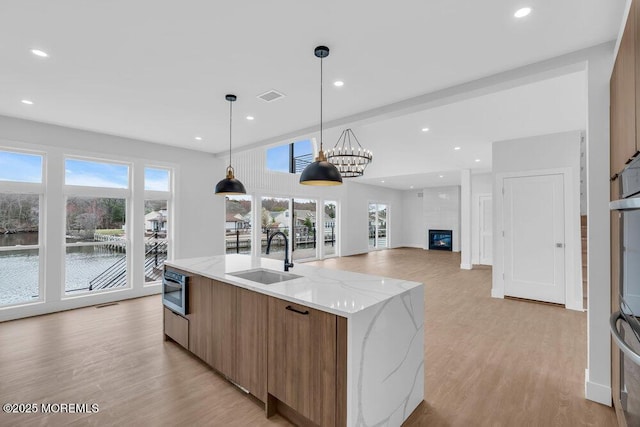 kitchen featuring modern cabinets, a sink, a kitchen island with sink, brown cabinetry, and light wood-style flooring
