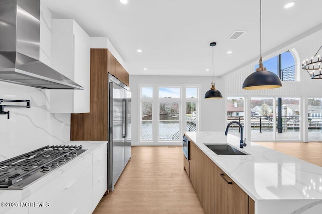 kitchen with wall chimney range hood, light wood-style floors, modern cabinets, appliances with stainless steel finishes, and a sink