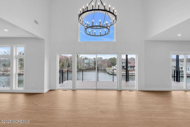 interior space featuring a notable chandelier, baseboards, a high ceiling, visible vents, and wood finished floors