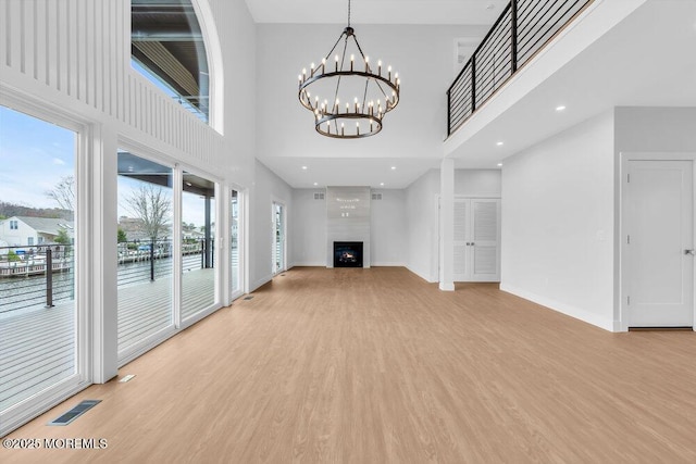 unfurnished living room featuring a large fireplace, visible vents, light wood finished floors, baseboards, and a notable chandelier