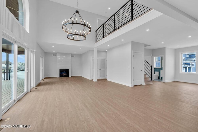 unfurnished living room with baseboards, recessed lighting, stairway, a large fireplace, and light wood-style flooring