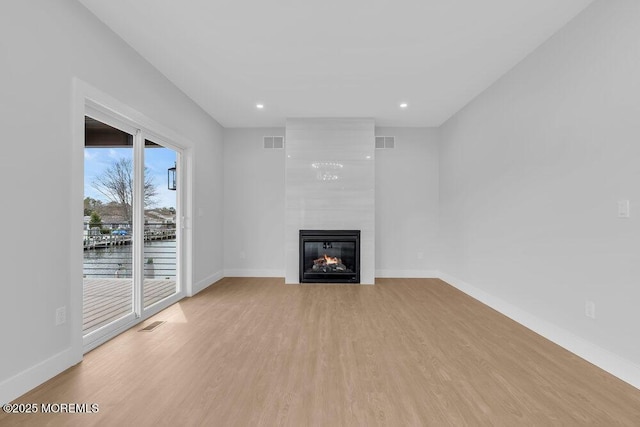unfurnished living room with light wood finished floors, baseboards, a large fireplace, and visible vents