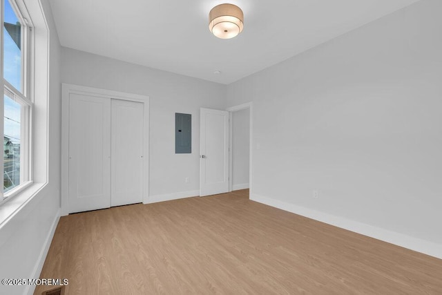 unfurnished bedroom featuring visible vents, a closet, baseboards, electric panel, and wood finished floors