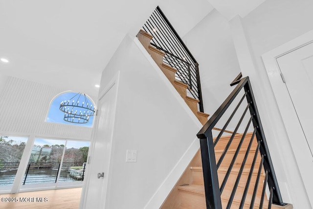 staircase featuring baseboards, a towering ceiling, an inviting chandelier, and wood finished floors