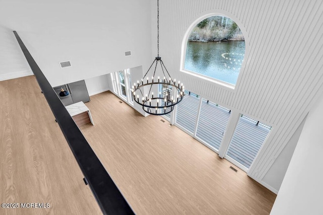 interior space featuring visible vents, a high ceiling, a water view, a chandelier, and wood finished floors